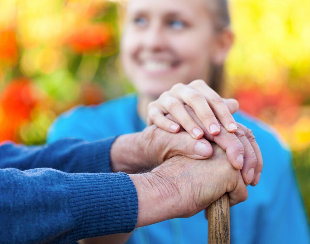 Volunteer with her hand on top of an elderly man's hands that are resting on a cane