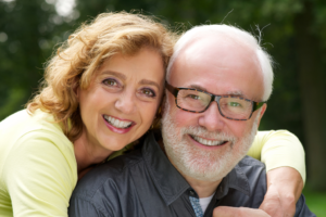 A woman with her arm around her husband who are both smiling who are in their sixties