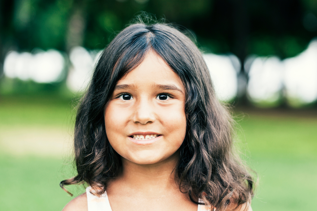 A smiling little girl with long brown hair and brown eyes